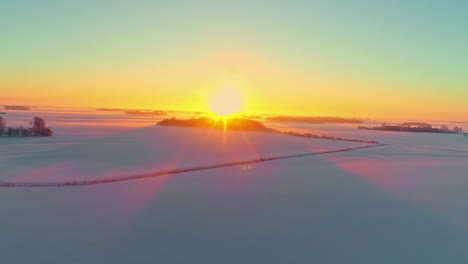 Aerial-drone-shot-over-white-snow-covered-farmland-with-sunrising-over-the-horizon-at-dawn
