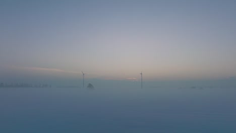 Luftbild-Von-Windkraftanlagen,-Die-Im-Windpark-Erneuerbare-Energie-Erzeugen,-Schneebedeckte-Landschaft-Mit-Nebel,-Sonniger-Winterabend-Mit-Goldenem-Stundenlicht,-Weites-Drohnenbild,-Das-Sich-Tief-Vorwärts-Bewegt