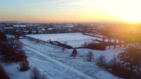 Beautiful-aerial-view-snow-covered-fields-and-park-at-sunset,-England
