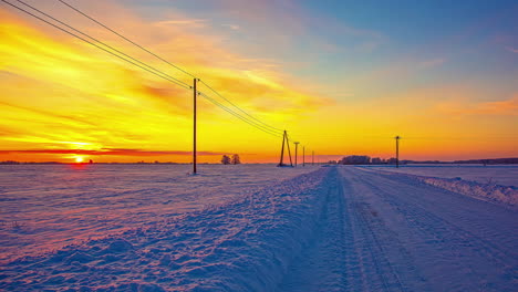 A-golden-sunrise-over-a-snowy-field-and-countryside-road-with-the-sunshine-reflecting-off-the-snow---time-lapse