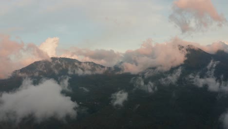 Luftdrohnenaufnahme-Von-Mit-Grünen-Wäldern-Bedeckten-Bergen,-Die-Bei-Sonnenuntergang-Und-Sonnenaufgang-Durch-Leichte-Wolkenfetzen-Fliegen