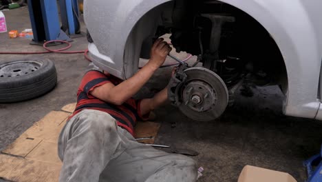 Ein-Erfahrener-Latino-Mechaniker,-Der-Auf-Dem-Boden-Liegt,-Repariert-Autobremsbeläge-Mit-Handwerkzeugen