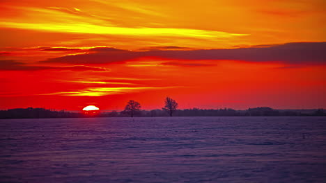 Time-lapse-shot-of-orange-colored-sun-ball-rising-up-behind-snowy-winter-field