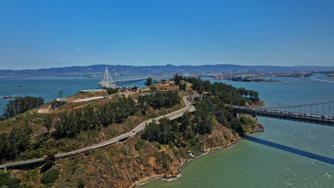 San-Francisco-California-Aerial-v103-heavy-traffic-on-bay-bridge-crossing-estuary,-vehicles-passing-through-tunnel-in-yerba-buena-island-with-oakland-cityscape-view---Shot-with-Mavic-3-Cine---May-2022