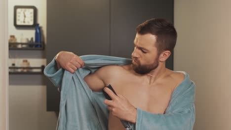 Portrait-of-young-man-using-antiperspirant-body-spray-in-bathrobe