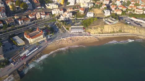 Overhead-aerial-view-of-people-enjoying-the-summer-at-beach-line,-waves-breaking-against-the-coastal-line-at-Poça-beach,-estoril,-cascais