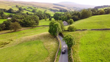 Single-car-drives-along-countryside-road-in-Summer-Yorkshire-Dales