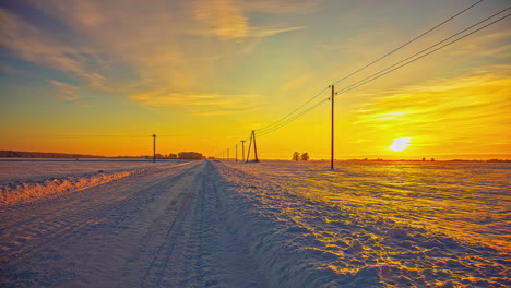 Zeitrafferaufnahme-Des-Wunderschönen-Orangefarbenen-Sonnenuntergangs-Am-Horizont-Des-Verschneiten-Ländlichen-Weges-Und-Der-Landschaft