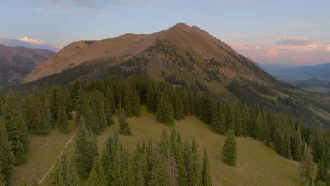 Aerial-over-trees-and-hiking-trail-and-towards-a-mountain-peak-in-Colorado