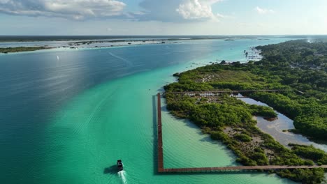 Aerial-view-of-a-boat-passing-the-pier-at-the-Area-natural-protegida-Parque-Laguna-de-Bacalar,-in-sunny-Mexico