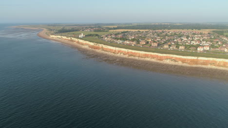 Establishing-Aerial-Drone-Shot-of-Old-Hunstanton-Orange-and-White-Cliffs-with-Lighthouse-and-Houses-on-Calm-Day-with-Small-Waves-at-Sunset-in-North-Norfolk-UK