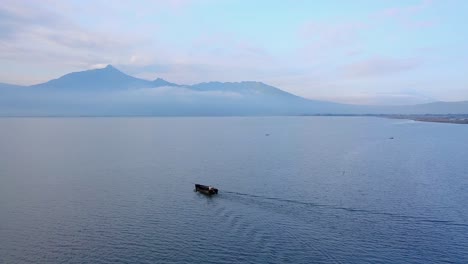 Toma-De-Un-Dron-Del-Barco-Siguiente-En-El-Lago-Con-Vistas-A-La-Montaña-En-El-Fondo---Lago-Rawa-Pening,-Indonesia