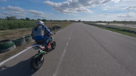 FPV-drone-POV-chasing-motorcycle-racer-speeding-around-Spanish-track-circuit,-Aerial-view