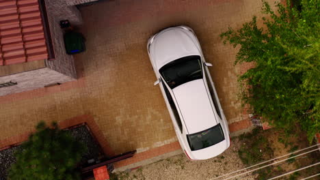 Aerial-top-down-of-white-sedan-car-entering-the-garage-for-parking-at-home