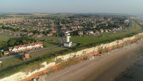 High-Establishing-Aerial-Drone-Shot-Rotating-Around-Old-Hunstanton-Lighthouse-above-Orange-and-White-Cliffs-and-Houses-with-Small-Sandy-Beach-at-Sunset-North-Norfolk-UK