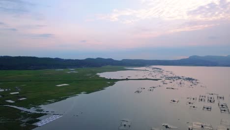 Aerial-flyover-view-of-fish-cages-and-rice-fields-with-mountains-in-background