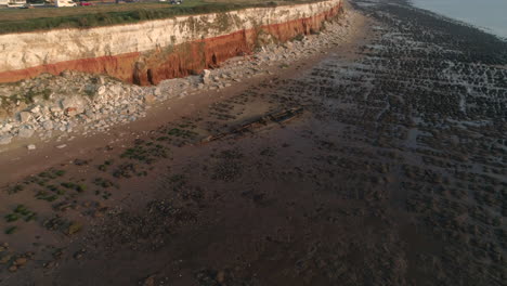 Aerial-Drone-Shot-Flying-Towards-The-Wreck-Of-The-Steam-Trawler-Sheraton-Old-Shipwreck-on-Old-Hunstanton-Beach-with-Orange-and-White-Stratified-Cliffs-at-Sunset-in-North-Norfolk-UK