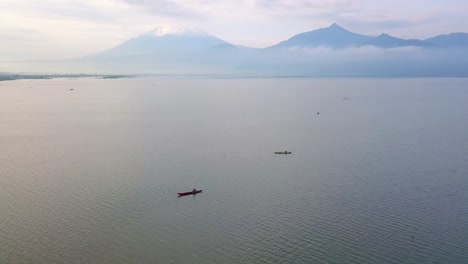 Orbit-drone-shot-of-traditional-wooden-boat-on-the-huge-lake-with-mountain-on-the-background---Rawa-Pening-Lake,-Indonesia