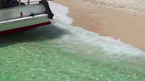 Tropical-water-waves-crashes-on-the-shore-of-Indonesian-island-with-boat-moored-up-on-the-orange-sand-beach