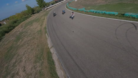Extreme-FPV-drone-chasing-motorcycles-on-racetrack-lap-corners,-Aerial-view