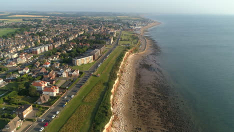 High-Aerial-Drone-Shot-Flying-Down-the-Line-of-Old-Hunstanton-Cliffs-with-Parallel-Road-and-Sandy-and-Rocky-Beach-will-Calm-Sea-Water-with-New-Hunstanton-in-the-Distance-North-Norfolk-UK
