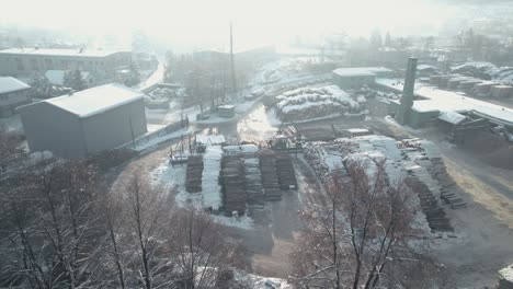 Aerial-shot-of-sawmill-with-wood-logs-and-tree-cranes-working-in-winter-season