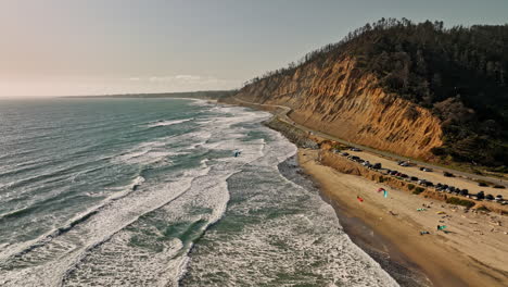 Davenport-California-Aerial-v2-flyover-post-wildfire-waddell-beach-and-creek-capturing-waves-hitting-the-shore,-coastal-highway-and-kite-boarders-flying-in-the-sky---Shot-with-Mavic-3-Cine---May-2022