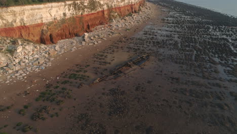 Pullback-Aerial-Drone-Shot-of-The-Wreck-Of-The-Steam-Trawler-Sheraton-Shipwreck-on-Old-Hunstanton-Beach-with-Orange-and-White-Cliffs-North-Norfolk-UK