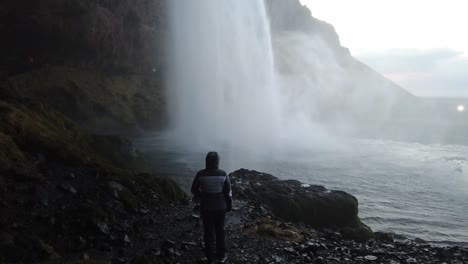 Girl-standing-and-looking-up-at-waterfall-in-cave-slowmotion-in-Iceland