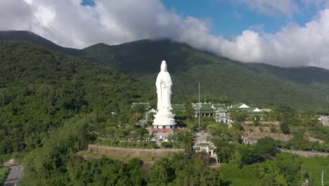Aerial-drone-view-of-tall-Lady-Buddha-statue-and-temples-with-huge-mountains-and-ocean-in-Da-Nang,-Vietnam
