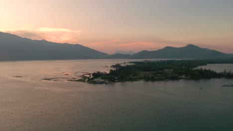 Aerial-sunset-flying-across-picturesque-and-peaceful-asian-landscape-with-lake,-mountains-and-fishing-village-in-Lang-Co,-Vietnam