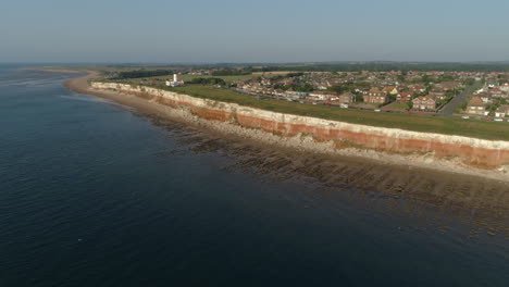 High-Establishing-Aerial-Drone-Shot-of-Old-Hunstanton-Stratified-White-and-Orange-Banded-Cliffs-with-Lighthouse-and-Sheraton-Steam-Trawler-Shipwreck-at-Sunset-in-North-Norfolk-UK