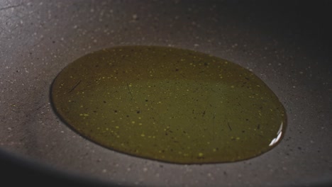 Slowly-puoring-cooking-oil-in-frying-pan,-macro-shot