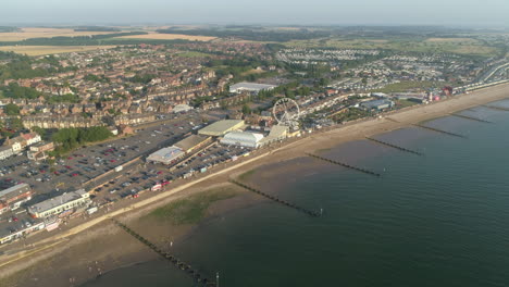 High-Establishing-Aerial-Drone-Shot-Flying-Forward-Over-Coastal-Seaside-Town-New-Hunstanton-with-Groynes-along-Sandy-Beach-and-Ferris-Wheel-and-Fun-Fair-with-Calm-Sea-with-Small-Waves-North-Norfolk-UK