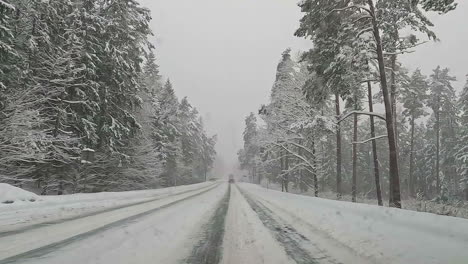 Windscreen-view-while-driving-through-a-beautiful-snow-covered-road-surrounded-by-coniferous-tree-forest-during-cold-winter-day