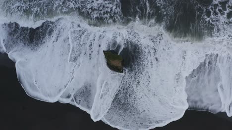 Aerial-top-down-black-sandy-beach-and-waves-crashing-against-Stapavik-rock-during-daytime