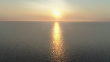 High-Aerial-Drone-Shot-of-Beautiful-Stunning-Sunset-at-Golden-Hour-Over-the-Sea-into-the-Sun-with-Amazing-Reflection-with-Small-Waves-and-Calm-Sea-in-UK