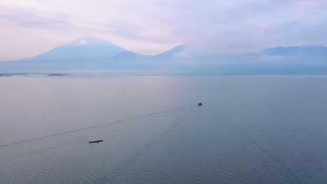 Traditionelles-Fischerboot,-Das-Morgens-Den-Hafen-Verlässt,-Um-Mit-Der-Silhouette-Der-Bergkette-Im-Hintergrund-Zu-Fischen---Indonesien