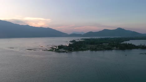 Aerial-sunset-flying-across-picturesque-and-peaceful-asian-landscape-with-lake,-mountains-and-fishing-village-in-Vietnam