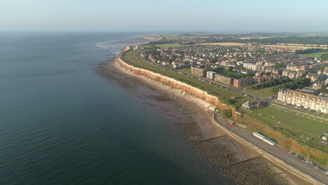 High-Establishing-Aerial-Drone-Shot-of-Old-Hunstanton-Orange-and-White-Cliffs-with-Houses-and-Lighthouse-in-Distance-at-Sunset-North-Norfolk-UK