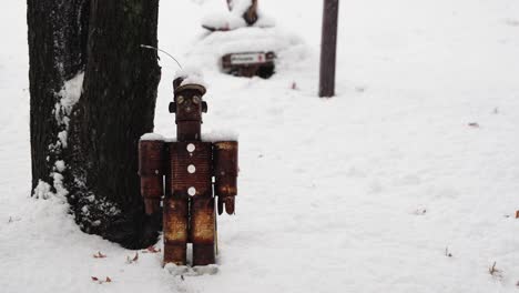 rusted-tin-can-character-sitting-in-the-snow-next-to-a-tree-on-a-snowy-day-in-the-middle-of-winter
