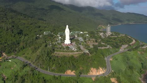Aerial-drone-flying-towards-tallest-Lady-Buddha-statue-and-temples-with-huge-mountains-and-ocean-in-Da-Nang,-Vietnam
