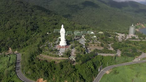 Antenne,-Die-Um-Hohe-Dame-Buddha-Statue-Und-Tempelturm-Mit-Riesigen-Bergen,-Atemberaubender-Küstenlinie-Und-Ozean-In-Da-Nang,-Vietnam-Kreist