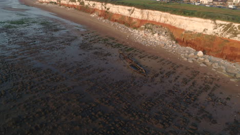 Aerial-Drone-Shot-of-The-Wreck-Of-The-Steam-Trawler-Sheraton-Old-Shipwreck-with-Orange-and-White-Banded-Old-Hunstanton-Cliffs-and-Lighthouse-at-Sunset-in-North-Norfolk-UK