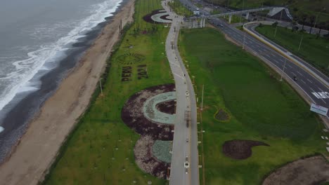 Green-grassy-park-with-a-long-walkway-by-the-ocean-shore-to-the-left-and-a-freeway-to-its-right