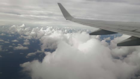 View-from-left-hand-airplane-window,-wing-view-over-white-cumulus-clouds-with-blue-ocean-below-and-cirrus-clouds-beyond