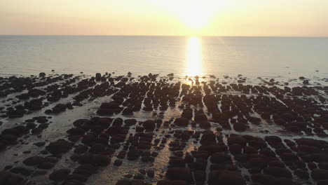 Aerial-Drone-Shot-At-Golden-Hour-Sunset-Descending-Over-Sandy-Beach-with-Rocks-Over-Calm-Sea-with-Small-Waves-in-Old-Hunstanton-North-Norfolk-UK-East-Coast