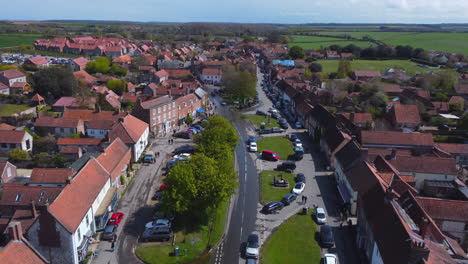 High-Aerial-Drone-Shot-Flying-Over-Beautiful-Old-Village-Burnham-Market-with-Red-and-White-Houses-on-Sunny-and-Cloudy-Day-with-People-in-the-Streets-in-North-Norfolk-UK