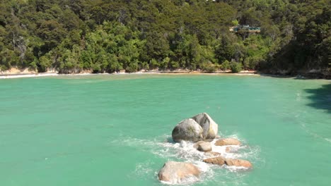 Aerial-clip-of-a-beach-in-the-Abel-Tasman-National-Park,-New-Zealand,-and-a-strange-rock-that-looks-like-a-split-apple-in-the-middle-of-the-sea