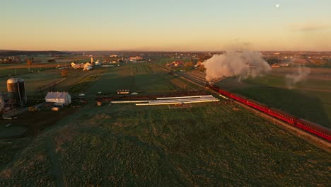 Drone-View-From-Above-and-Behind-of-a-Steam-Engine-Approaching-Blowing-Lots-of-Smoke-at-Sunrise-Traveling-Thru-the-Farmlands-on-Fall-Morning